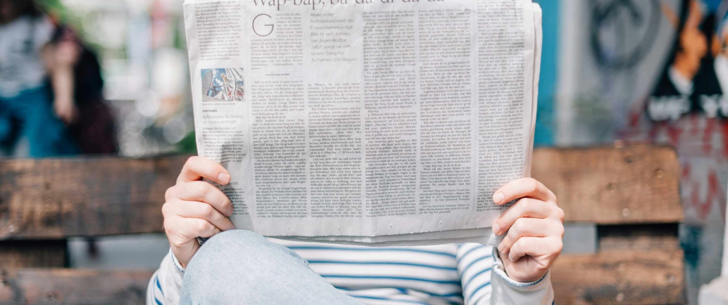 person holding up a newspaper and reading it