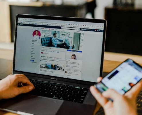Person browsing social media on a laptop while holding a smartphone.