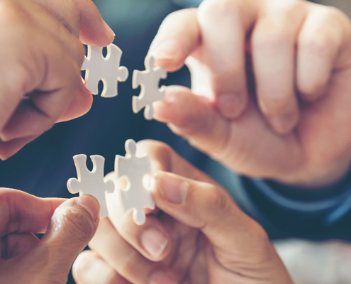 pr team holding puzzle pieces in agency office, view of hands only