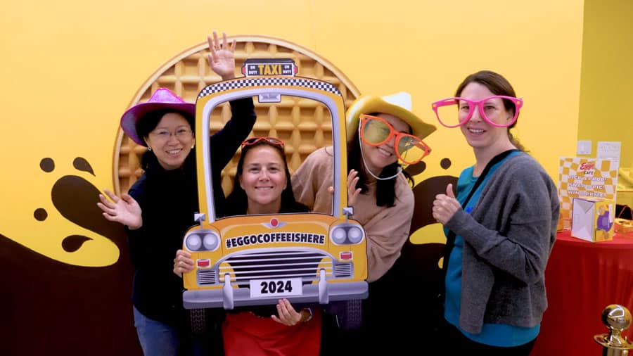 friends posing with large glasses and fake car in front of large waffle wall art at Kellogg's Eggo Coffee PR event