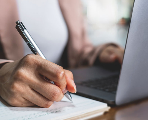 journalist sitting at laptop and using pad and paper to write a pr notes for a branding campaign