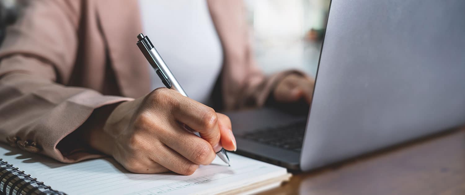 journalist sitting at laptop and using pad and paper to write a pr notes for a branding campaign