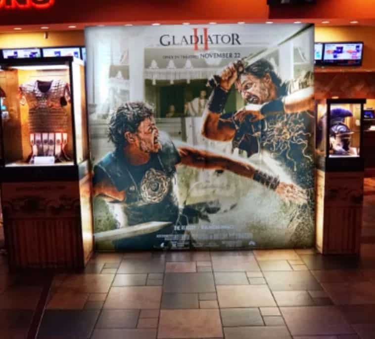 gladiator II movie poster in theater, with movie props on either side in glass cases, for pr campaign for film’s release